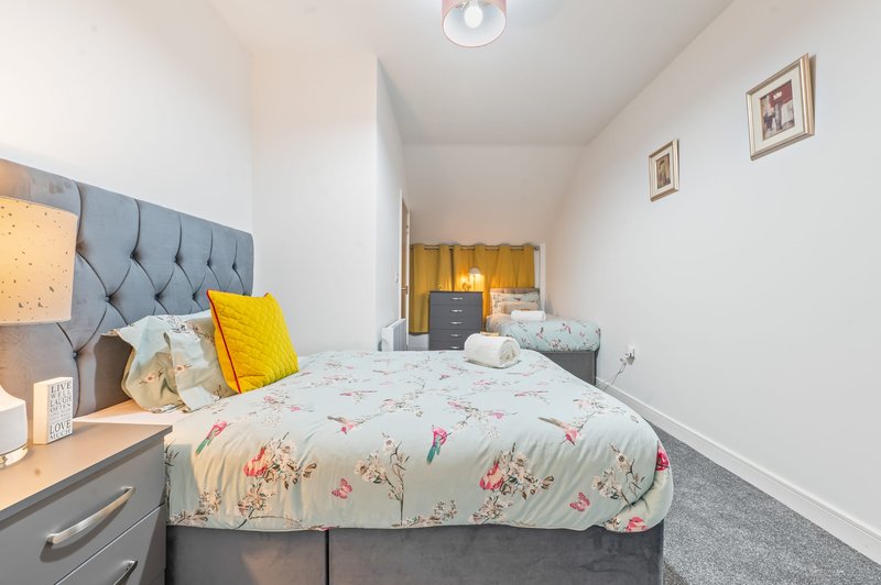 Bright bedroom with double bed, tufted headboard, yellow accent pillow, and bedside lamp