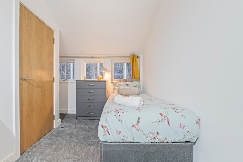 Bright bedroom with single bed, wooden door, dark dresser and ensuite bathroom visible