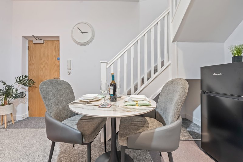 Open-plan kitchen and dining area with round white table, grey chairs, and staircase