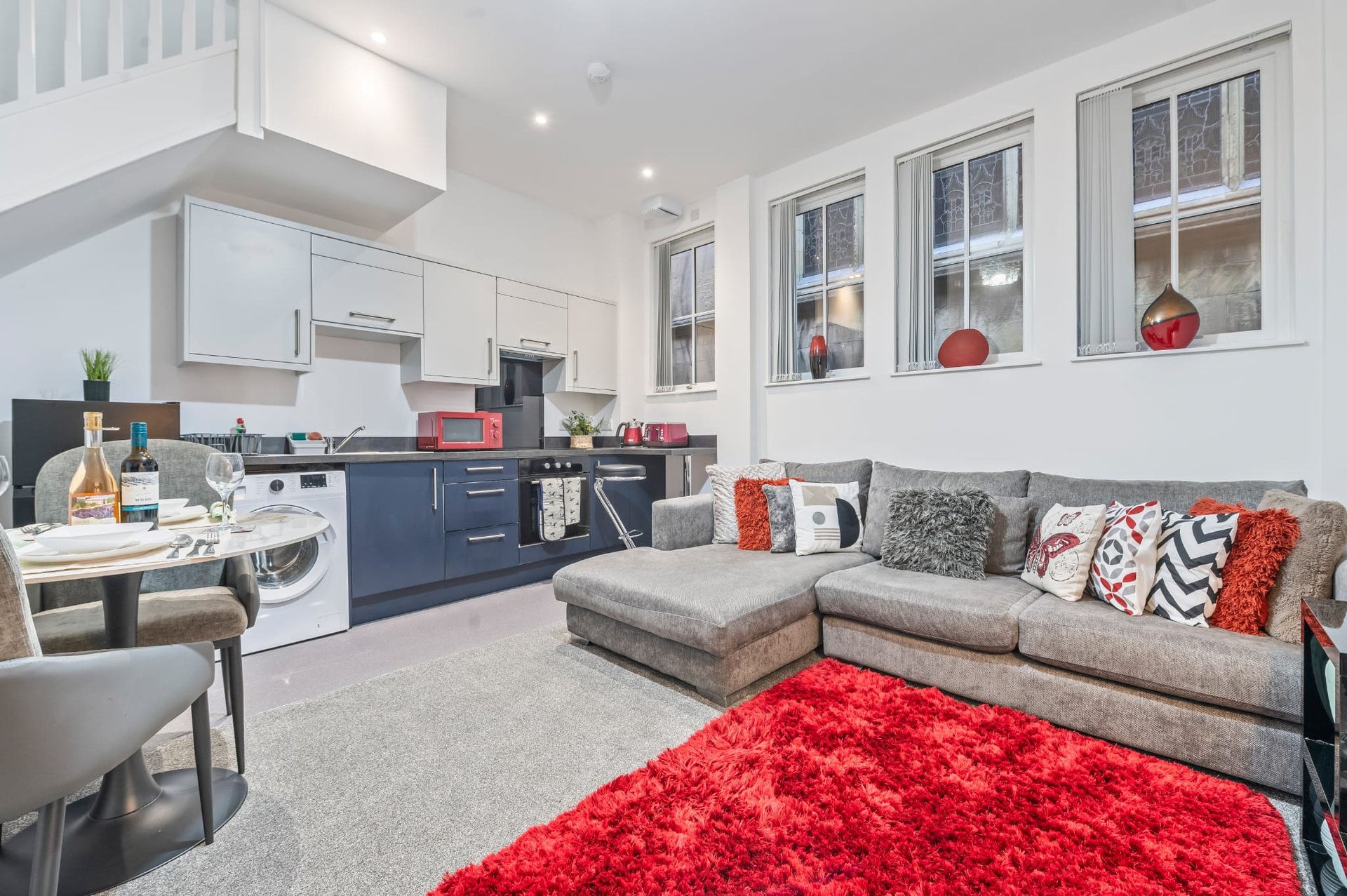 Open-plan kitchen and living area with navy cabinetry, gray sofa, and red accent rug