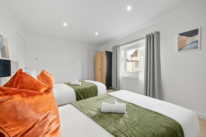 Modern bedroom with twin beds, orange and green bedding, grey curtains and wood flooring