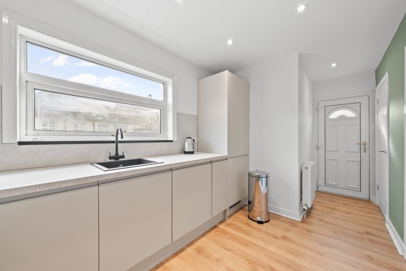 Modern kitchen with cream cabinetry, stainless steel sink, window overlooking street, wooden flooring