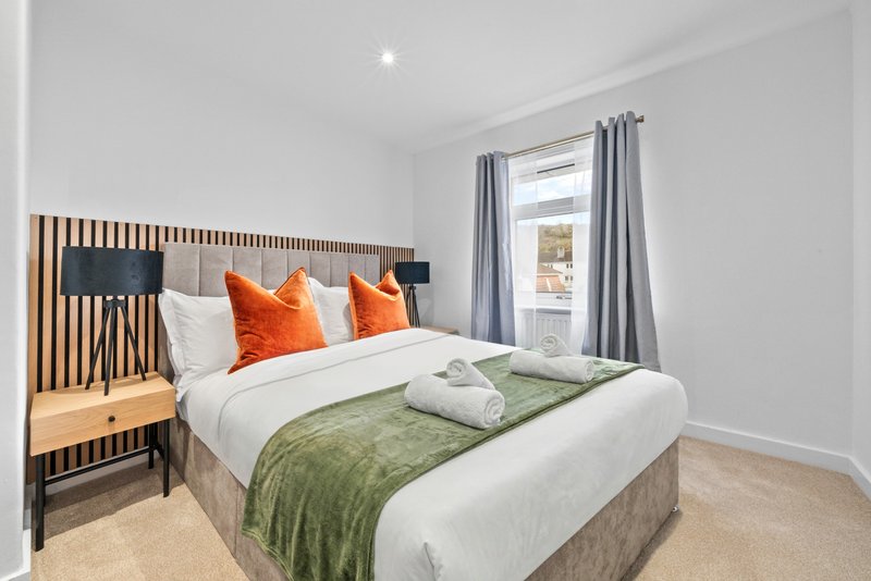 Modern bedroom with double bed, orange cushions, wooden headboard and grey curtains