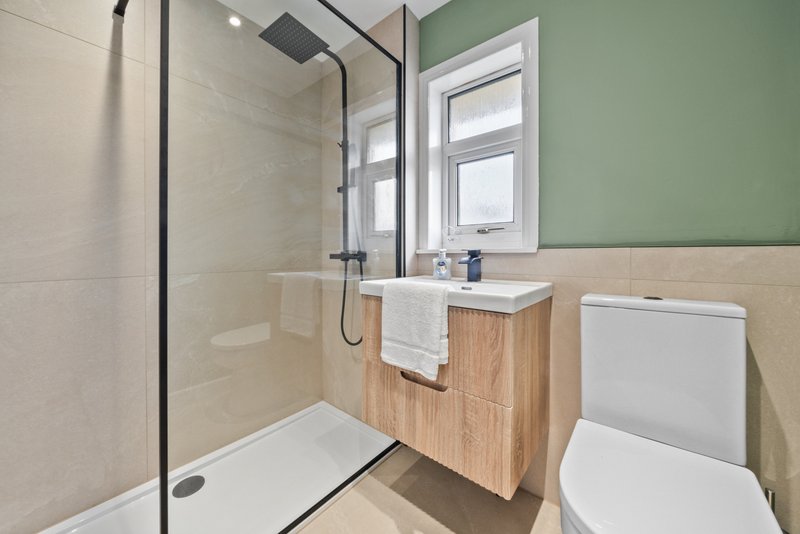 Modern bathroom with walk-in shower, wooden vanity, toilet, and green accent wall