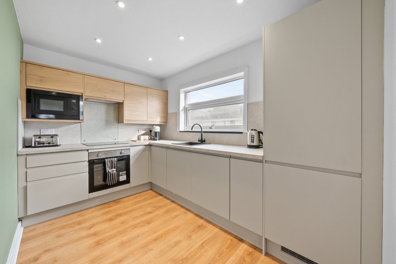 Modern kitchen with light wood and grey cabinetry, wooden flooring and window