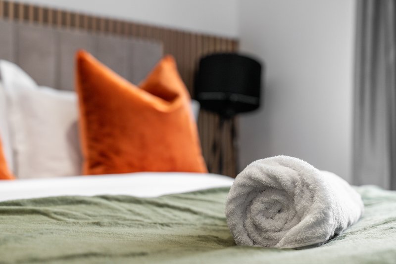 Bedroom with rolled towel on bed, orange cushion, and headboard
