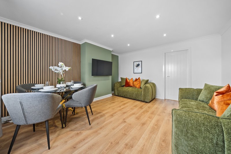 Modern open-plan living area with dining table, green upholstered sofa, wall-mounted TV and wooden flooring