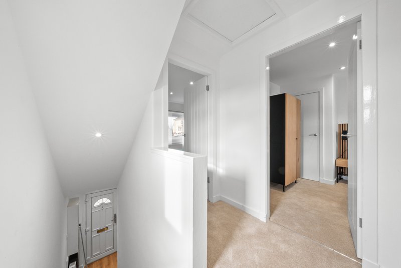 Bright hallway with white walls, wooden flooring, and multiple doorways leading to rooms