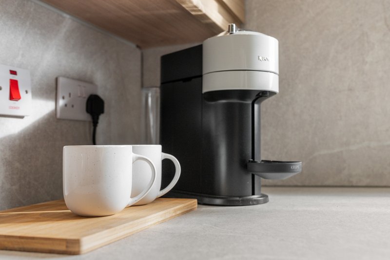 Kitchen counter with coffee maker, white mugs on wooden board and outlet