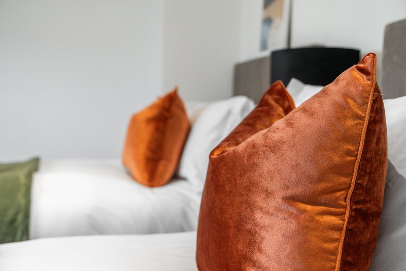 Bedroom with white bedding, orange velvet cushions and upholstered headboard