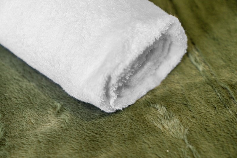 Rolled white towel on olive green carpet or rug