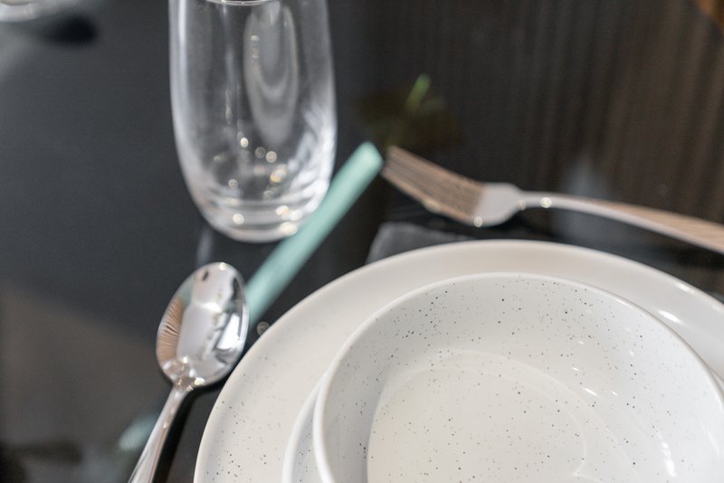 Place setting with white speckled plates, glass, and utensils on dark table