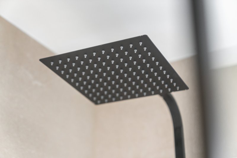 Black square rainfall showerhead mounted on white ceiling with curved pipe visible
