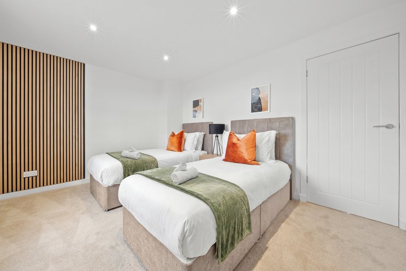 Modern bedroom with two single beds, green bedding, orange cushions, wood-paneled accent wall