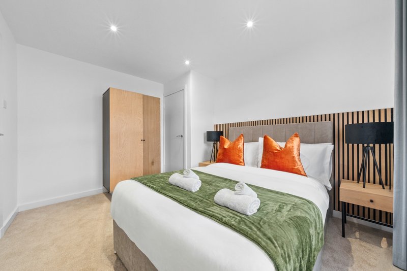 Modern bedroom with double bed, green throw, orange pillows and wooden wardrobe