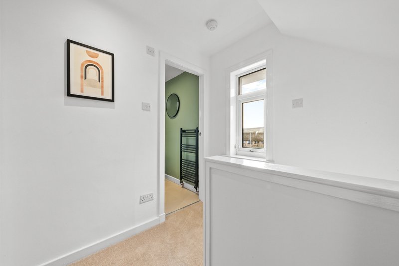 Bright hallway with white walls, framed wall art, doorway to green bathroom, and window with countryside view