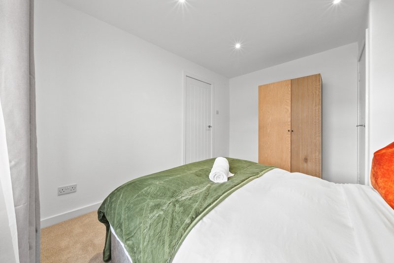 Bright bedroom with double bed, green throw, wooden wardrobe and white walls