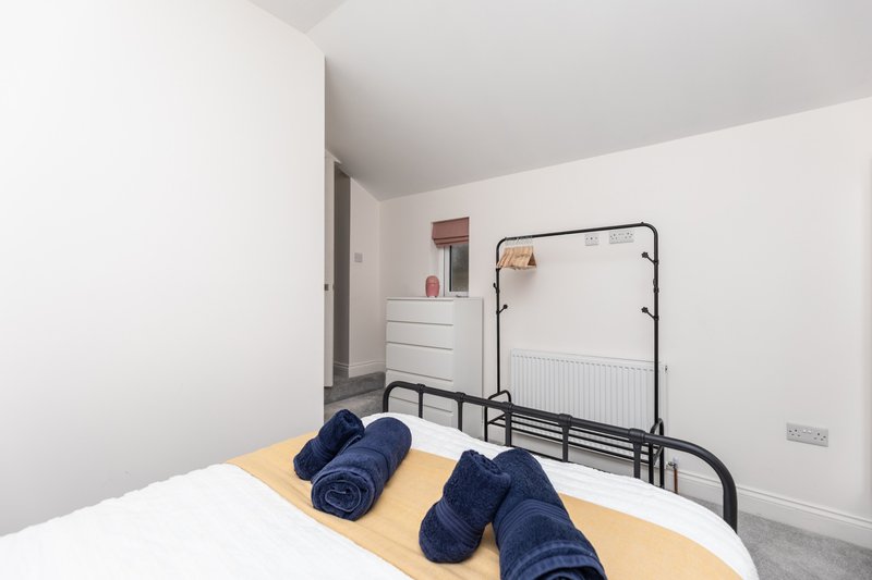 Bedroom with double bed, rolled towels, clothes rail, white dresser, and radiator
