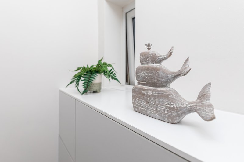 White dresser with potted plant and three decorative wooden whale figurines