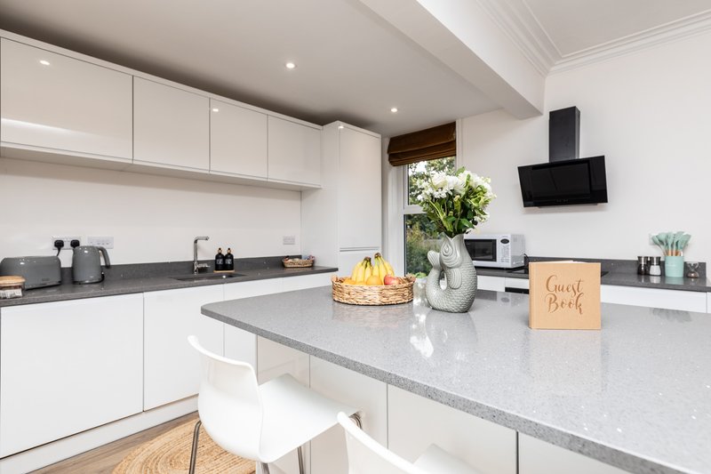 Modern white kitchen with grey countertops, island seating, and garden view
