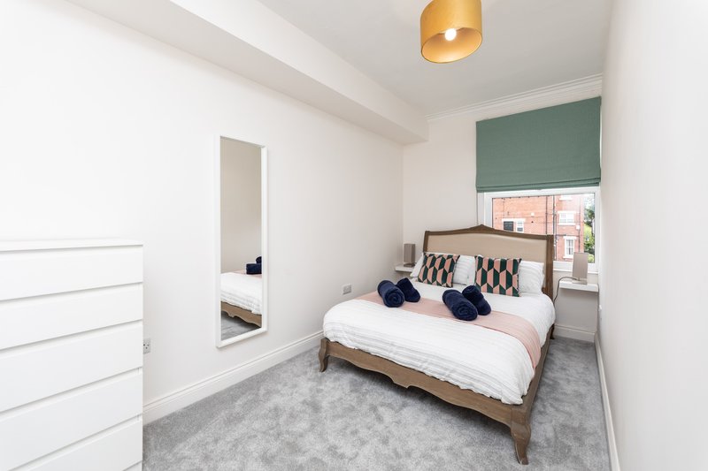 Modern bedroom with double bed, wooden frame, patterned headboard cushions, gray carpet and pendant light