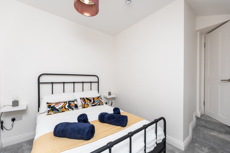 Modern bedroom with metal-frame bed, navy rolled towels, patterned pillows, and copper ceiling light