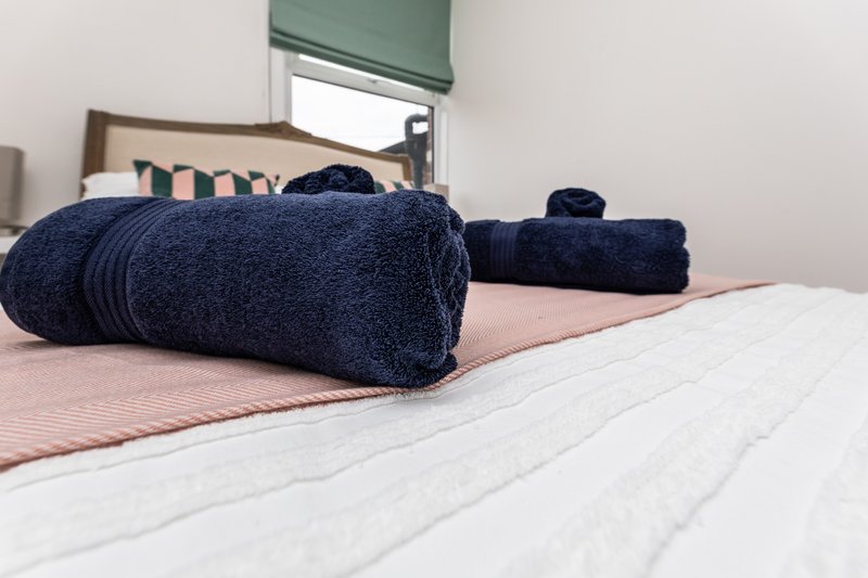 Bedroom with rolled navy towels on bed, striped bedding, wooden frame and green blind