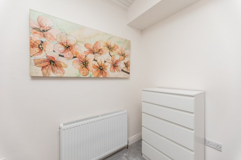 Small bedroom with white radiator, white chest of drawers, and floral wall art
