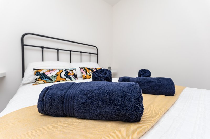 Bedroom with metal frame bed, rolled navy towels, patterned pillows and white bedding