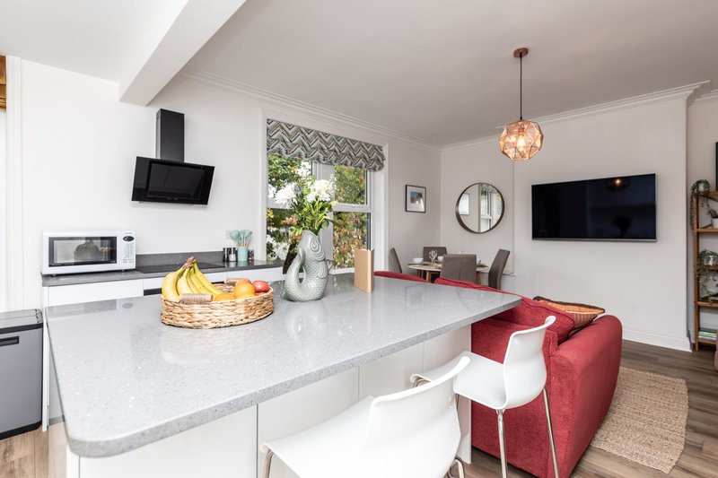 Open-plan kitchen and living area with white countertop, red sofa, pendant light and wall-mounted TV