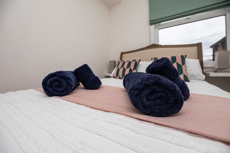 Bedroom with double bed, dark blue towel rolls, pink throw, and patterned cushions