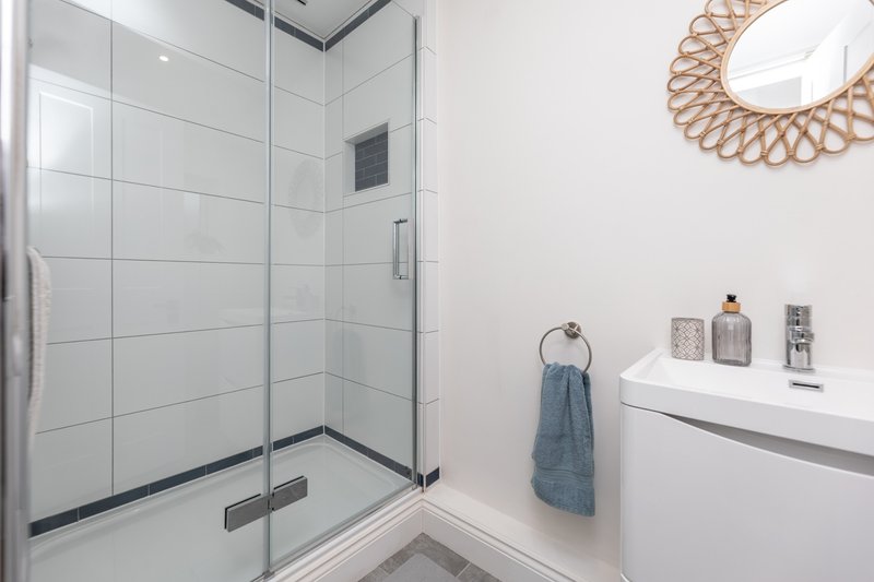 Modern bathroom with walk-in shower, white vanity, woven mirror and towel rack
