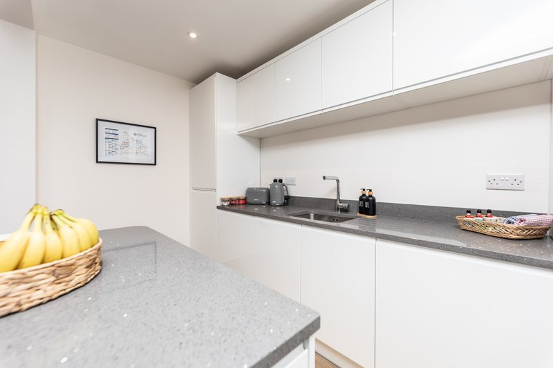 Modern white kitchen with gray countertops, built-in appliances, and fresh fruit basket