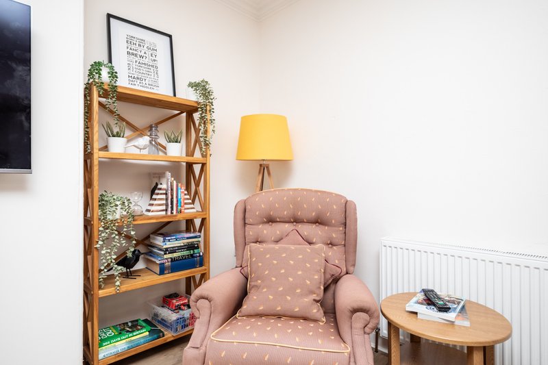 Living room corner with upholstered armchair, wooden bookshelf, yellow lamp, and side table