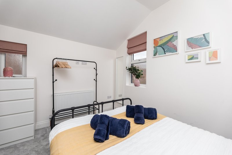 Bright bedroom with double bed, black metal frame, white bedding, and rolled blue towels