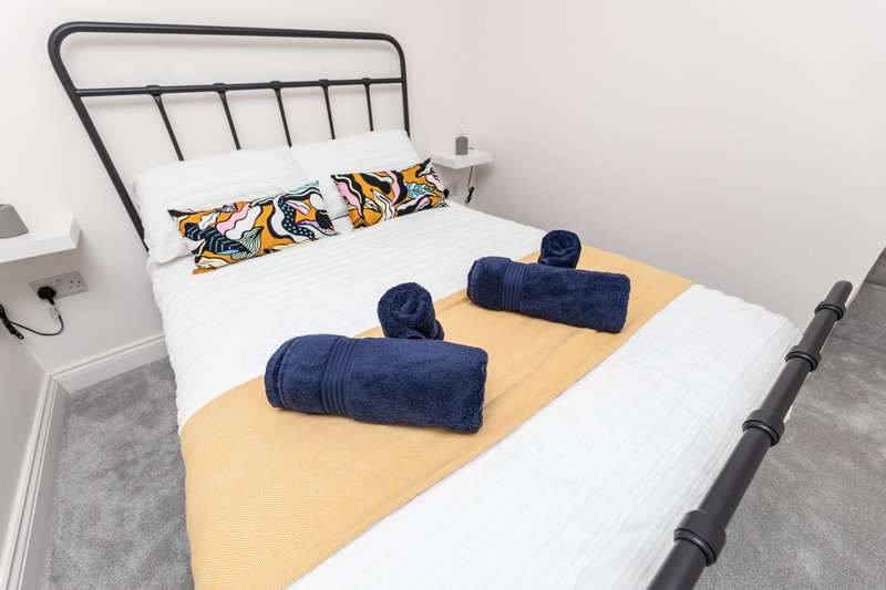 Bedroom with metal-frame bed, white bedding, decorative pillows and rolled navy towels