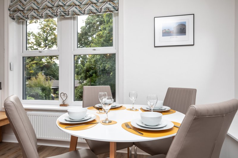 Dining room with round white table, grey upholstered chairs, place settings, and garden views through large windows