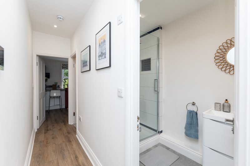Modern hallway with wooden flooring and bathroom entrance showing shower enclosure and vanity