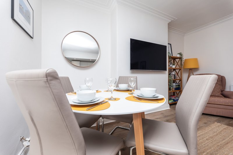 Modern dining area with round white table, upholstered chairs, place settings and round mirror