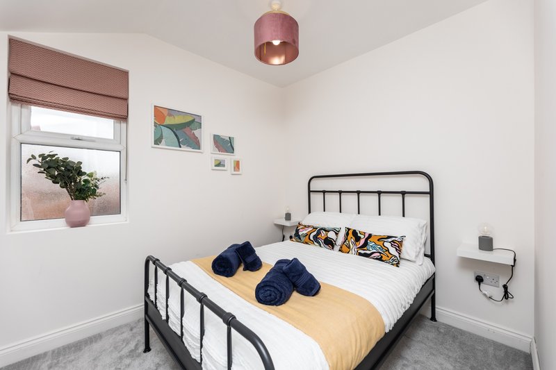 Bright bedroom with black metal bed frame, white bedding, yellow throw, and blue cushions