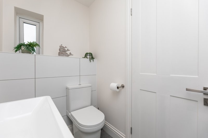 Modern bathroom with white subway tile, toilet, bathtub, and wall-mounted shelving with plants