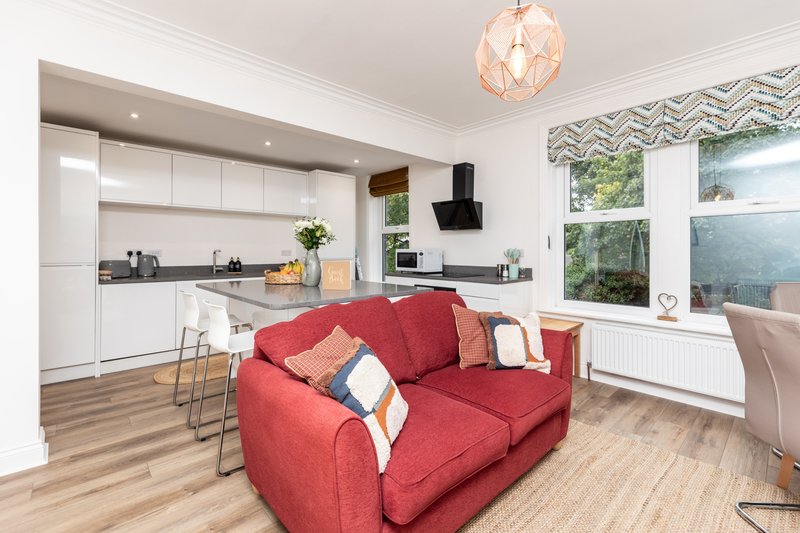 Open-plan living room with red sofa, kitchen, pendant light and large windows