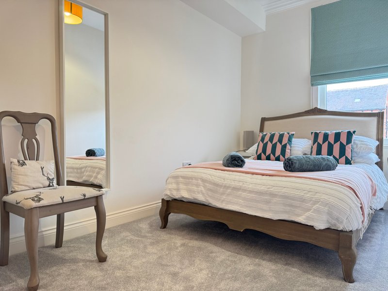 Bedroom with wooden bed frame, patterned pillows, full-length mirror and upholstered chair