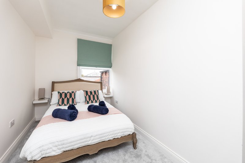 Small bedroom with wooden bed, white bedding, navy pillows and green window blind