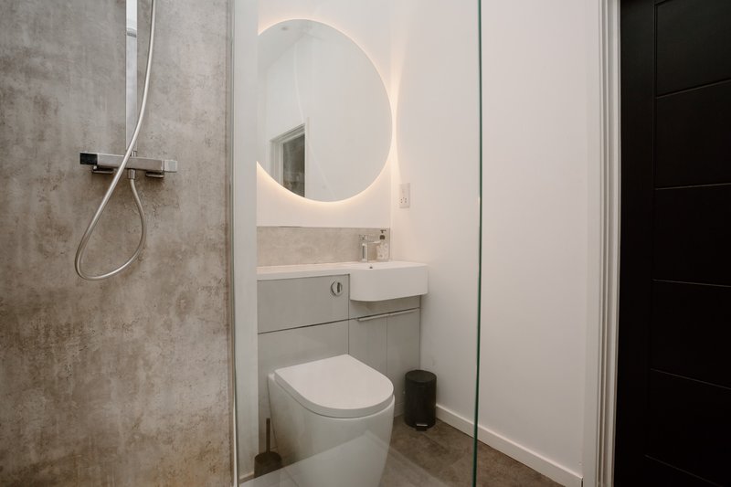 Modern bathroom with illuminated round mirror, white sink vanity, toilet and shower area