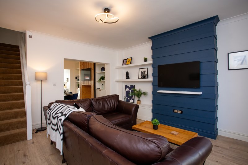 Living room with brown leather sofas, blue feature wall with TV, wooden shelving and staircase visible
