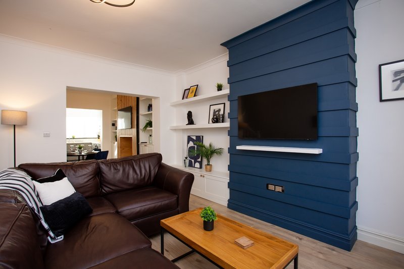 Modern living room with brown leather sofa, blue shiplap accent wall and wall-mounted TV