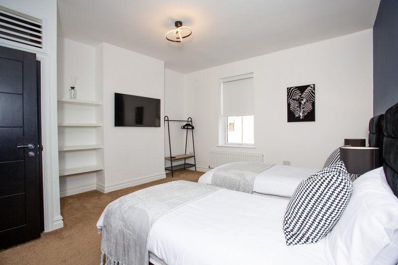 Bright modern bedroom with two single beds, wall-mounted TV, built-in shelving and window