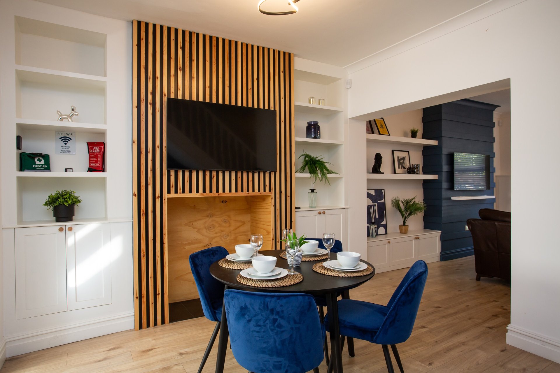 Open-plan dining and living area with blue velvet chairs, round table, wooden flooring and built-in shelving