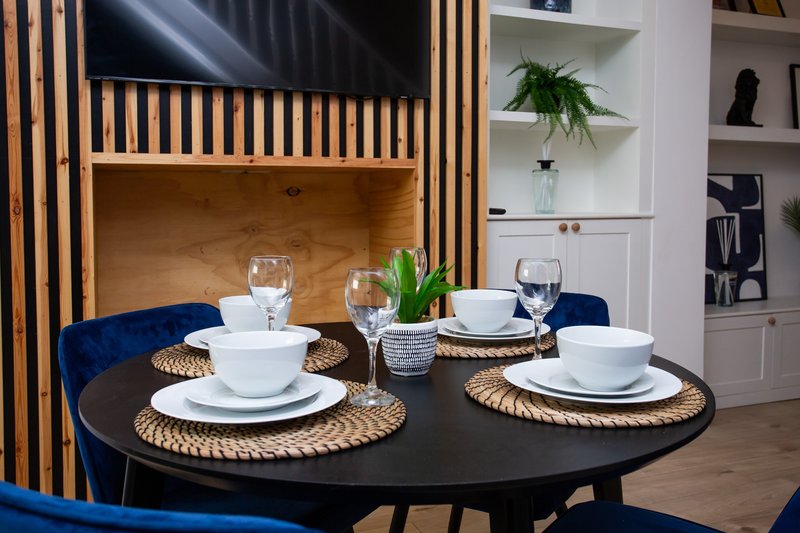 Modern dining area with round black table, blue velvet chairs, place settings and decorative shelving